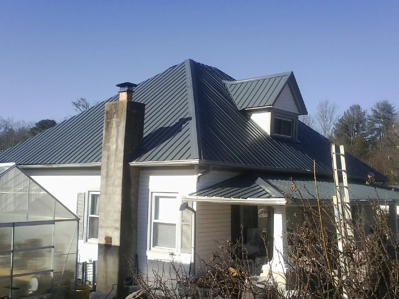 Dark blue standing seam metal roof on a white farmhouse with dormer — Slate & Tile Roof Repair by Roofing Brothers in Cardinal