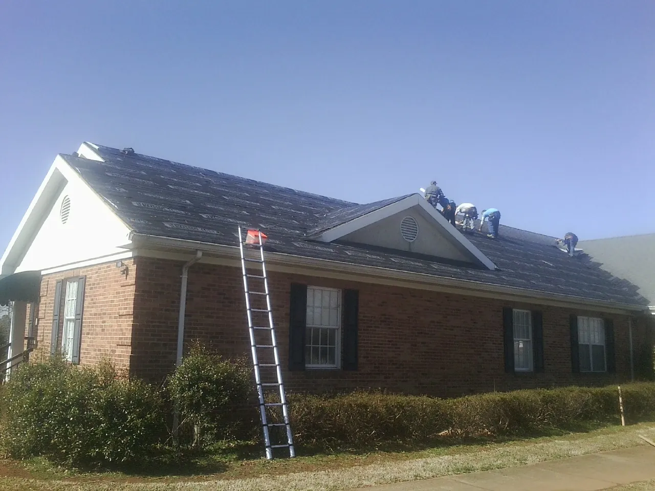 Crew tearing shingles off a brick ranch roof with a ladder set — Metal Roof Repair work by our crew in Cardinal