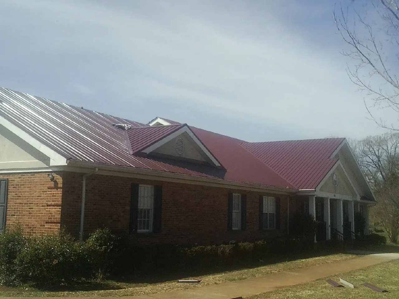 Red metal roof with gabled entries on a long brick building, from a Hail Damage Roof Repair job in Cardinal