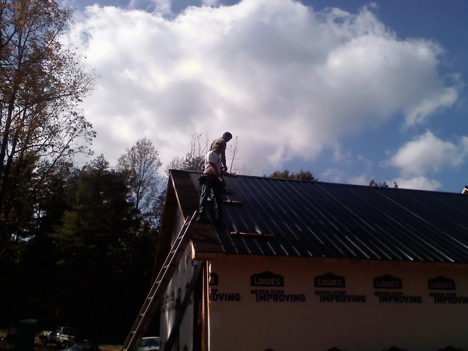 Roofer fastening dark metal panels high against a cloudy sky, from a Roof Inspection job in Cardinal