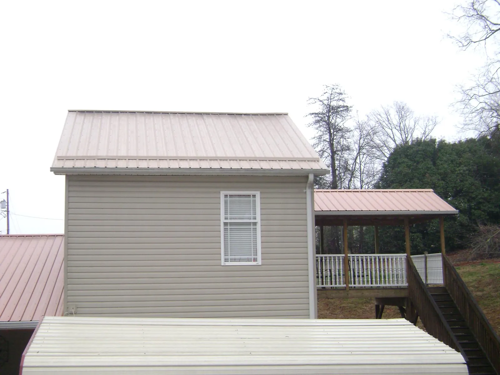 Tan metal roofs on a two story addition and attached porch, from a Roof Replacement job in Cardinal