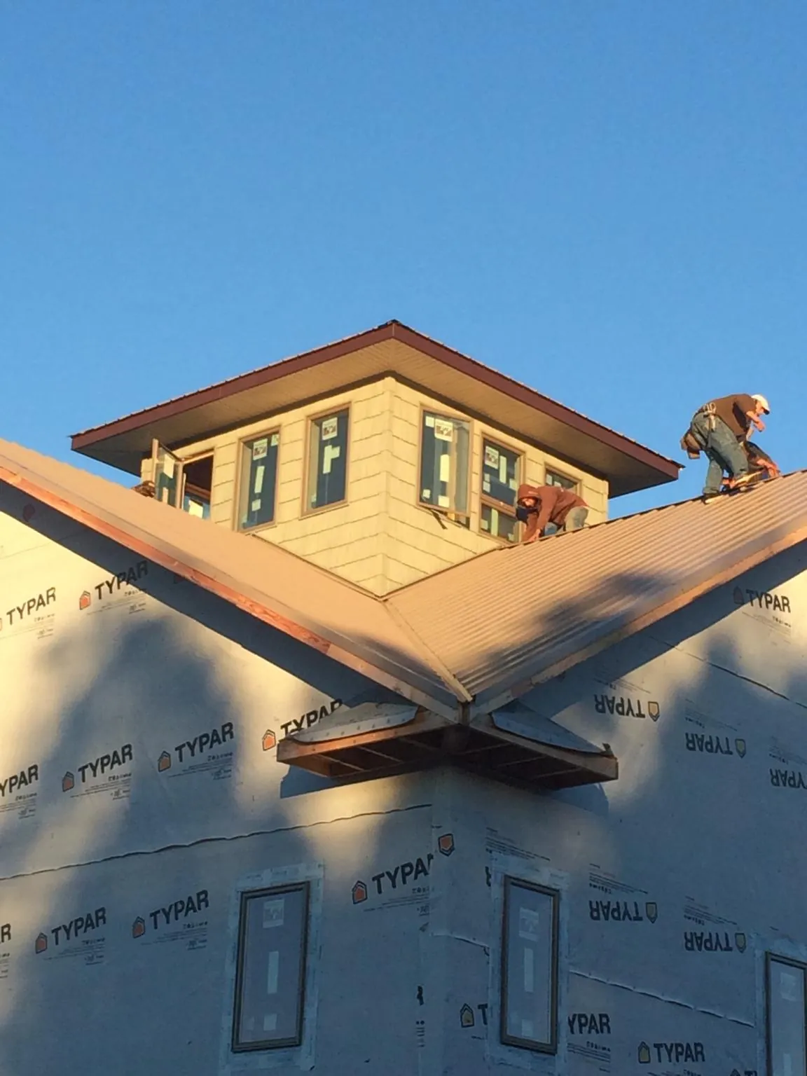 Roofers working around a rooftop cupola on a new metal roof at sunset — Roof Waterproofing in Cardinal by Roofing Brothers